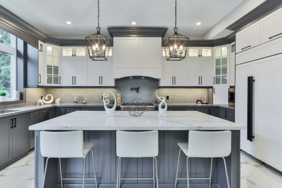 Modern kitchen with gray cabinetry, marble island, and pendant lighting.