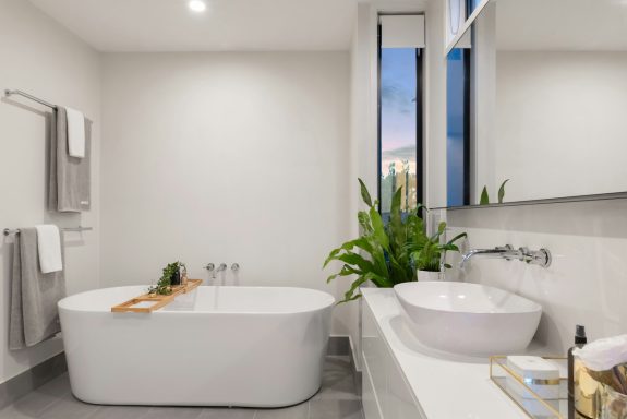 Modern bathroom featuring a freestanding tub, vessel sink, and large window with plants.