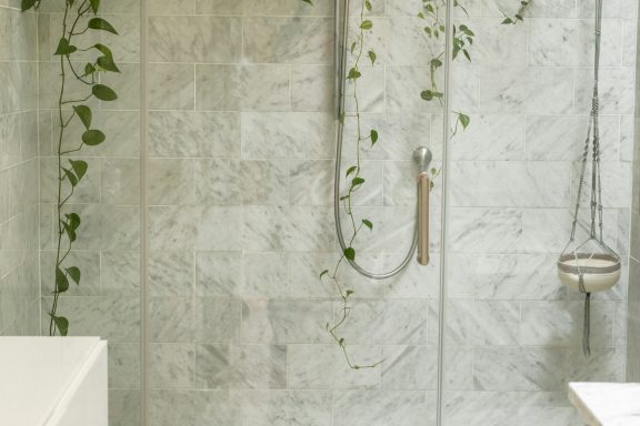 Modern bathroom featuring marble walls, a shower, and trailing green plants.