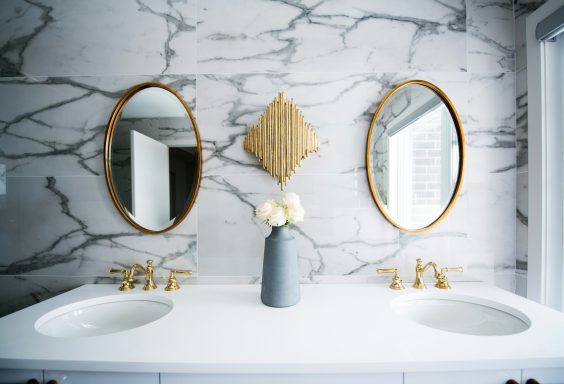 Modern bathroom with dual sinks, gold fixtures, round mirrors, and marble walls.