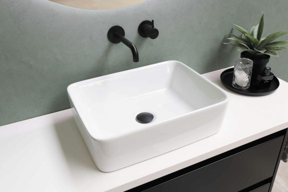 Square white sink on a countertop with black fixtures and a small plant.