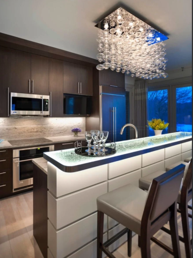 Modern kitchen with dark cabinetry, a sparkling chandelier, and a sleek countertop.