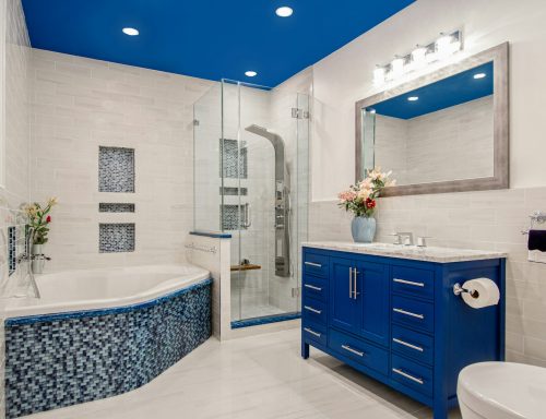 Modern bathroom with blue accents, glass shower, and a large bathtub with mosaic tiles.