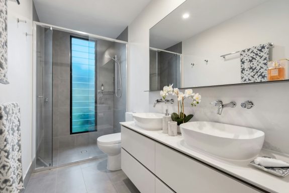 Modern bathroom featuring double sinks, a glass shower, and decorative accents.